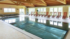 Une piscine intérieure dotée d’un plafond en bois et de grandes fenêtres laissant entrer la lumière du soleil.
