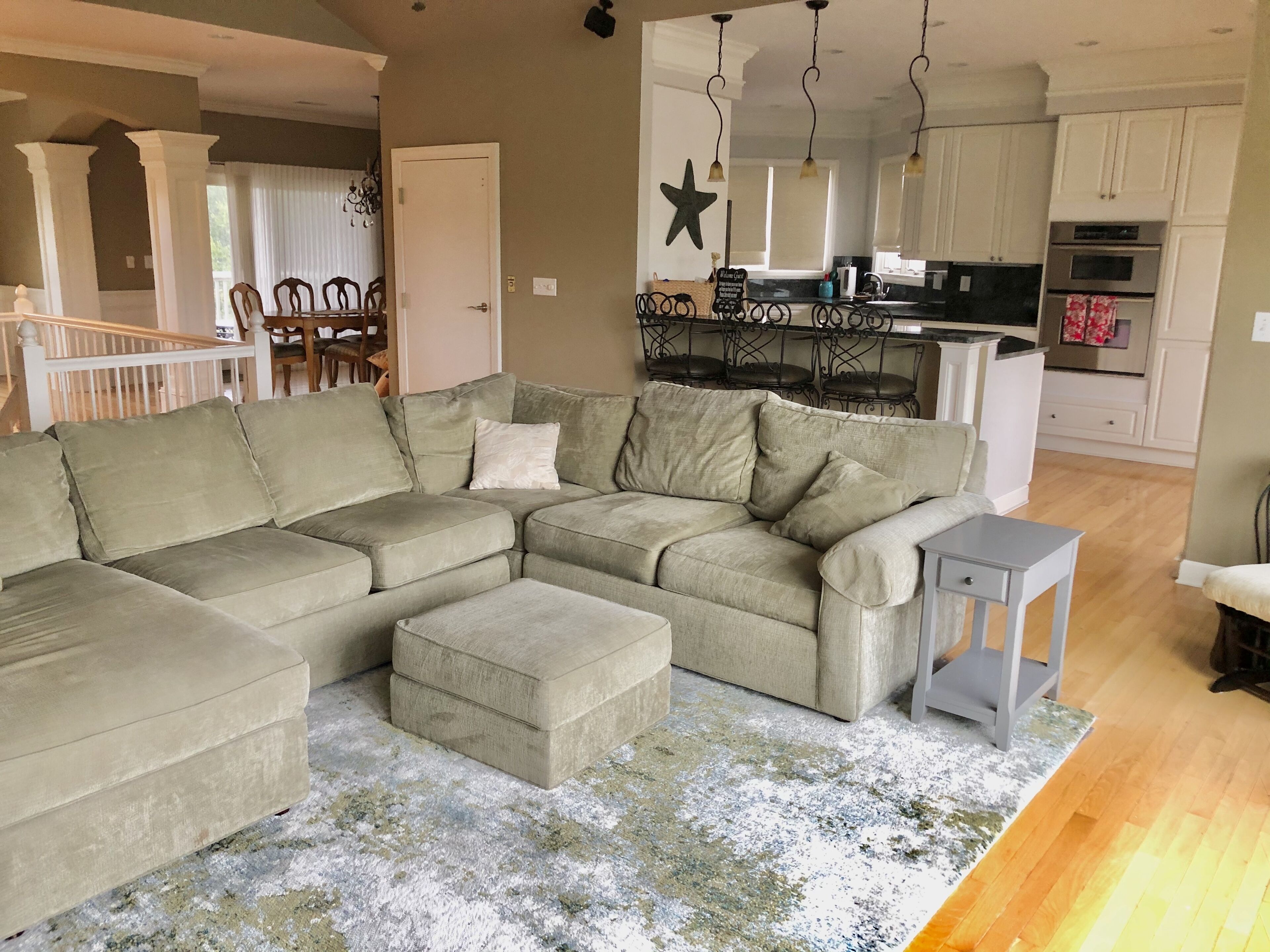 A living room with a sectional sofa, a small table, and a kitchen in the background.