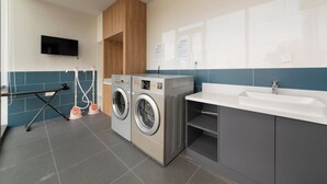 A modern bathroom with a large sink, two wall-mounted washing machines, and a television mounted on the wall.