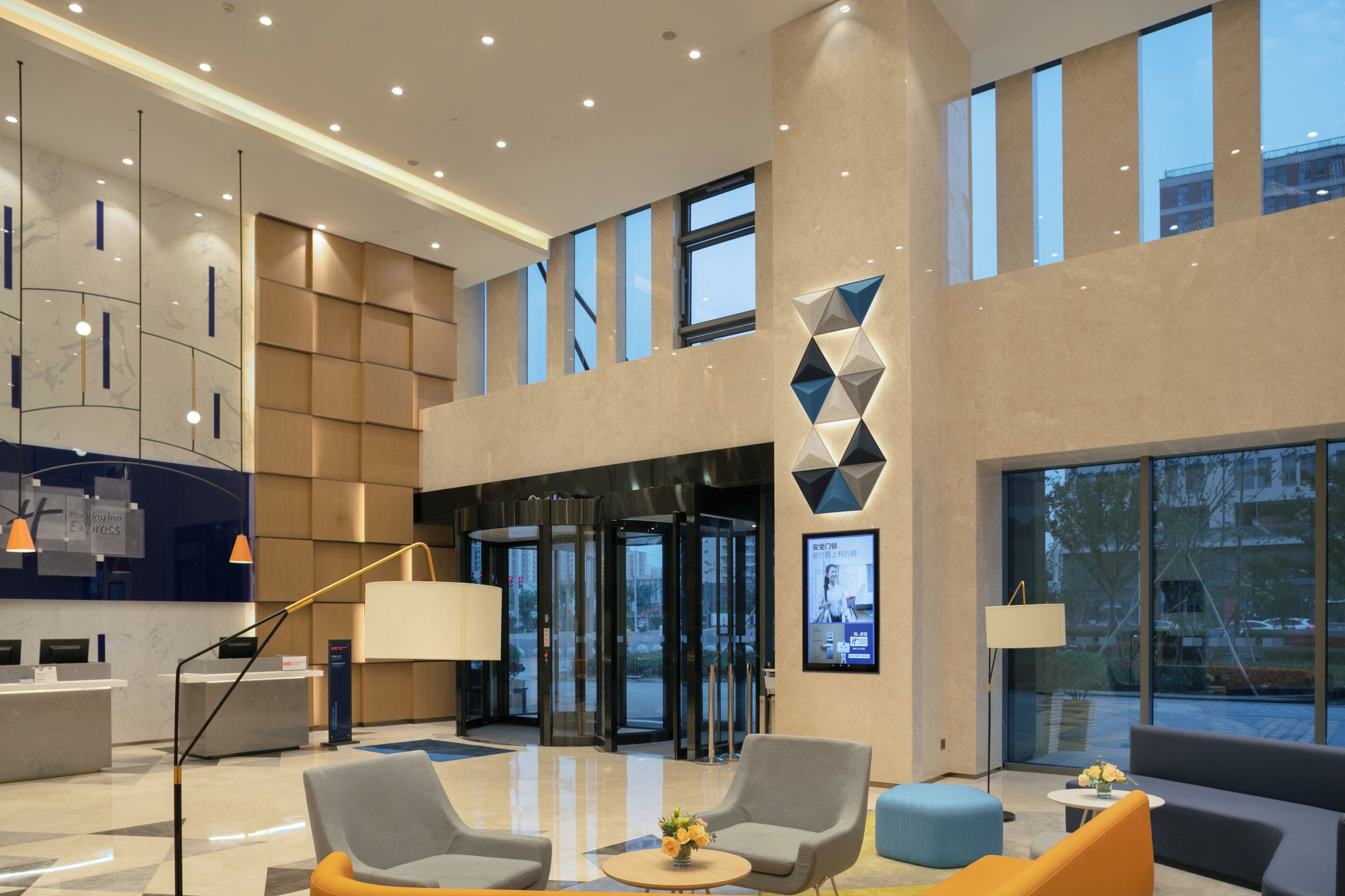 A modern hotel lobby with a reception desk, seating area, and large windows.