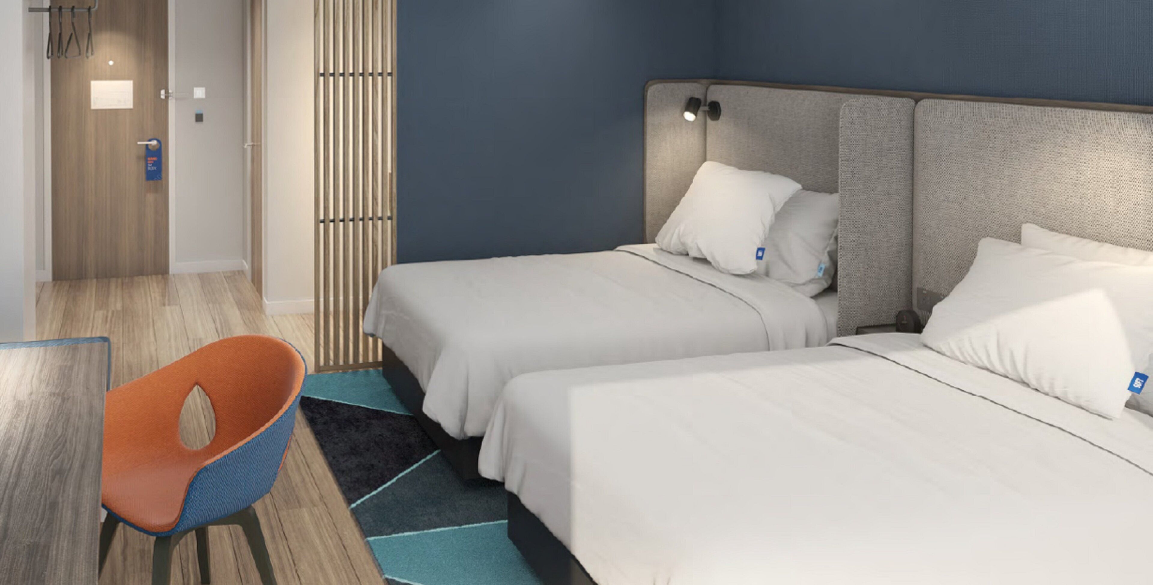 A hotel room with two beds, a chair, and a wooden floor.