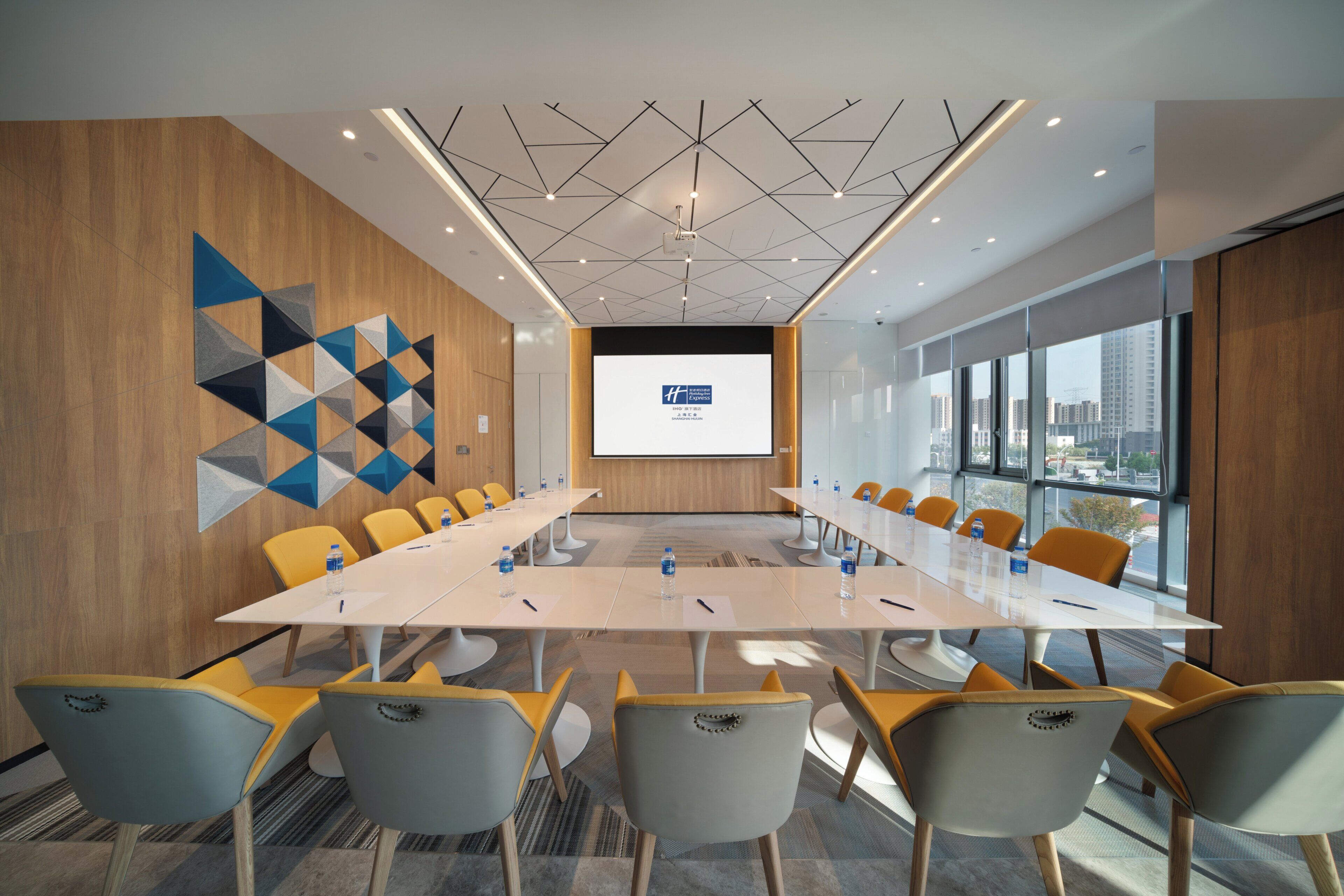 A conference room with a long table, multiple chairs, a projector screen, and a city view through large windows.