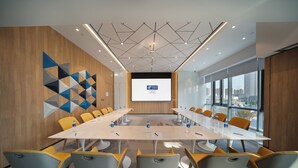 A conference room with a long table, multiple chairs, a projector screen, and a city view through large windows.