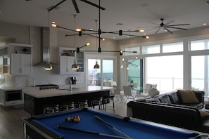 A modern kitchen with a pool table, bar area, and large windows offering a view.