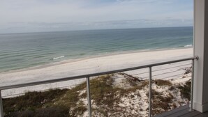 Vista de la playa desde un balcón con barandilla, océano y costa distante.