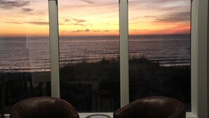 Una habitación con un amplio ventanal con vistas al océano al atardecer.
