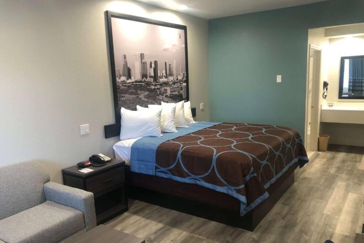 A hotel room with a bed, a nightstand, a chair, and a wall-mounted TV.