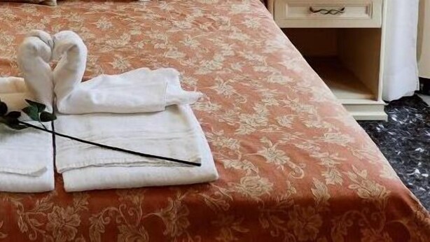 Un lit bien fait, avec une couvre-lit à motifs floraux et des serviettes disposées en forme de cœur, une rose et un élastique noir pour les cheveux.