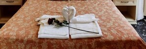 A neatly made bed with a floral bedspread and towels arranged in a heart shape, a rose, and a black hair tie.