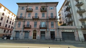 Un bâtiment rose avec un volet fermé au rez-de-chaussée, portant l’inscription « Nuovo Shopping Center ».