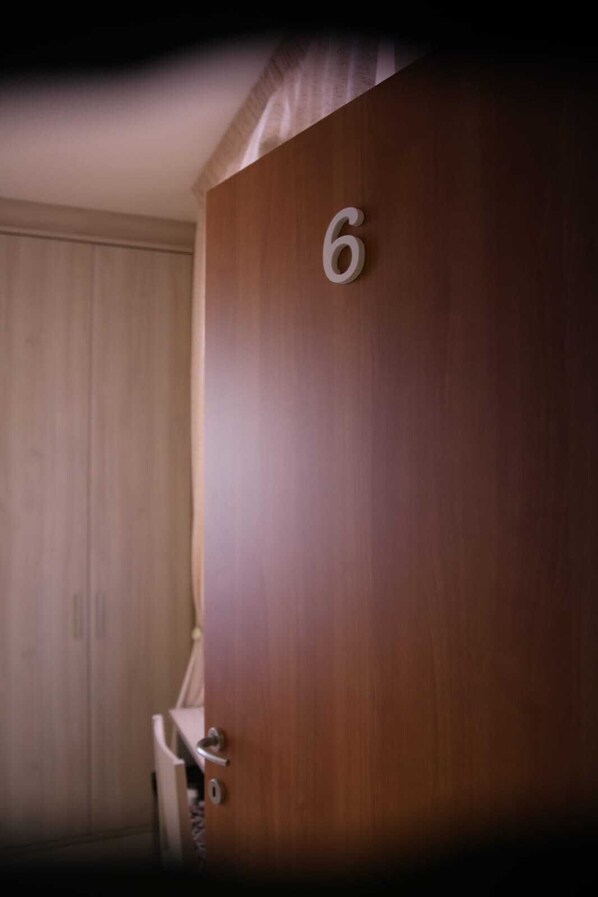 A wooden door with the number 6 on it, a door handle, and a partial view of a white door frame.