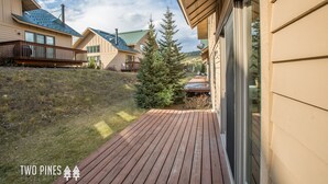 A wooden deck with a view of a hillside and a house with a green roof. - Lush Ski-in/out Home! Wood Fireplace, Grill, Walk to Resort! (Big Sky)