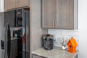 Una cocina con un refrigerador negro, una cafetera y una casa de pájaros decorativa.