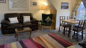 Una sala de estar acogedora con un sofá de cuero marrón, un sillón verde, una mesa de centro de madera y una mesa de comedor con sillas.