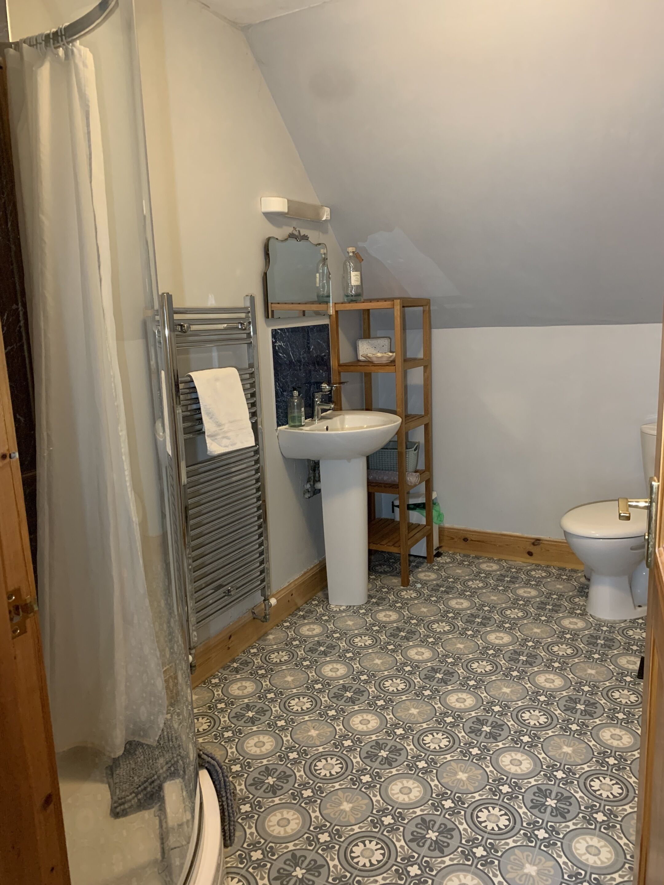 Un baño con piso de baldosas, un lavamanos blanco, un estante de madera y un inodoro.