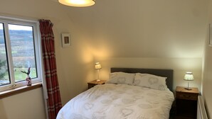 Un dormitorio con cama, dos lámparas de noche, una ventana con cortinas, un cuadro en la pared y un radiador.