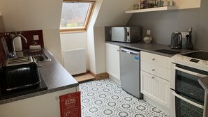 Una cocina compacta con ventana, microondas, hervidor, lavavajillas y estufa.