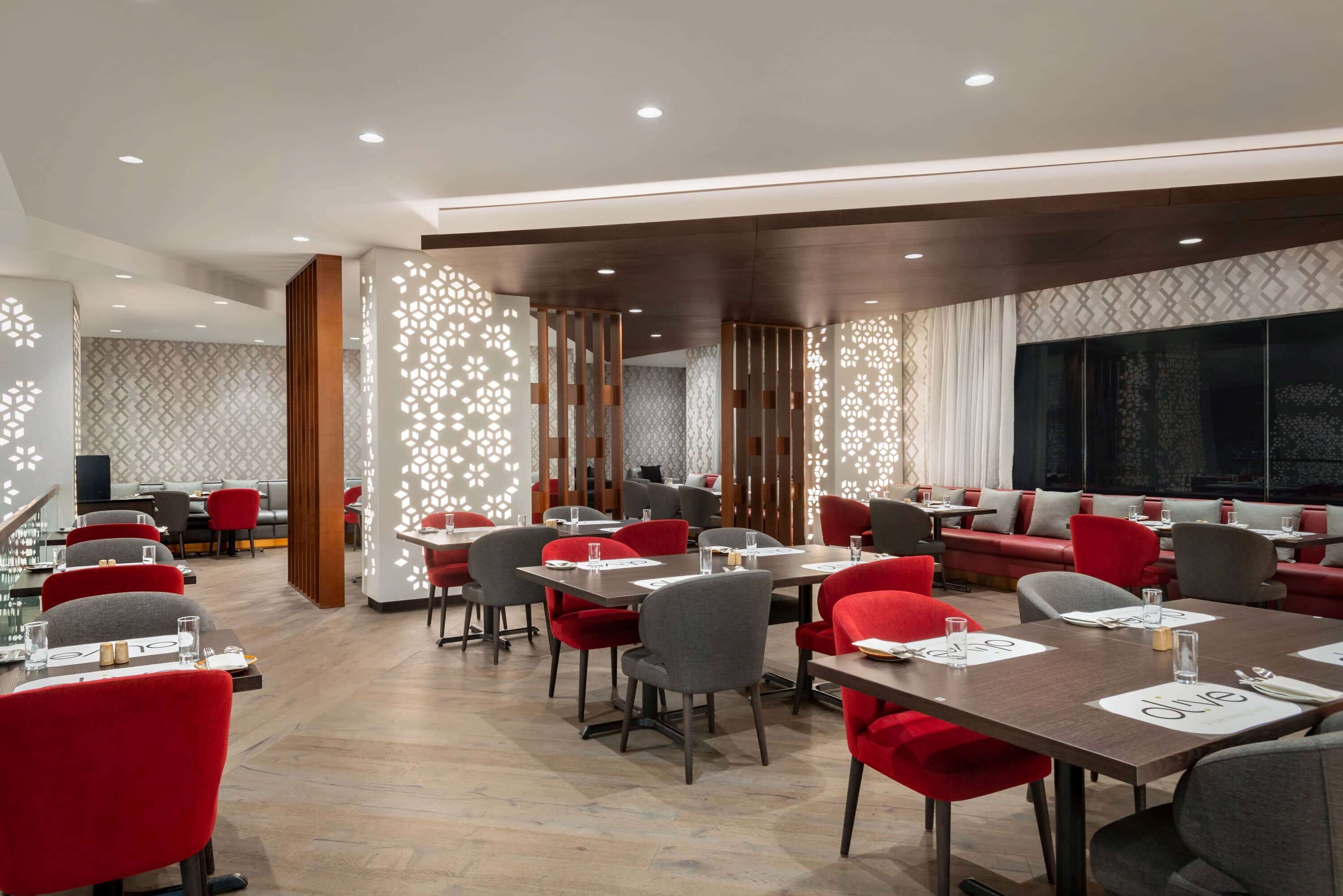 A modern restaurant with red and grey chairs, wooden tables, and patterned walls.