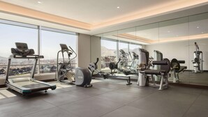 A modern gym with various exercise equipment, large windows, and a city view.