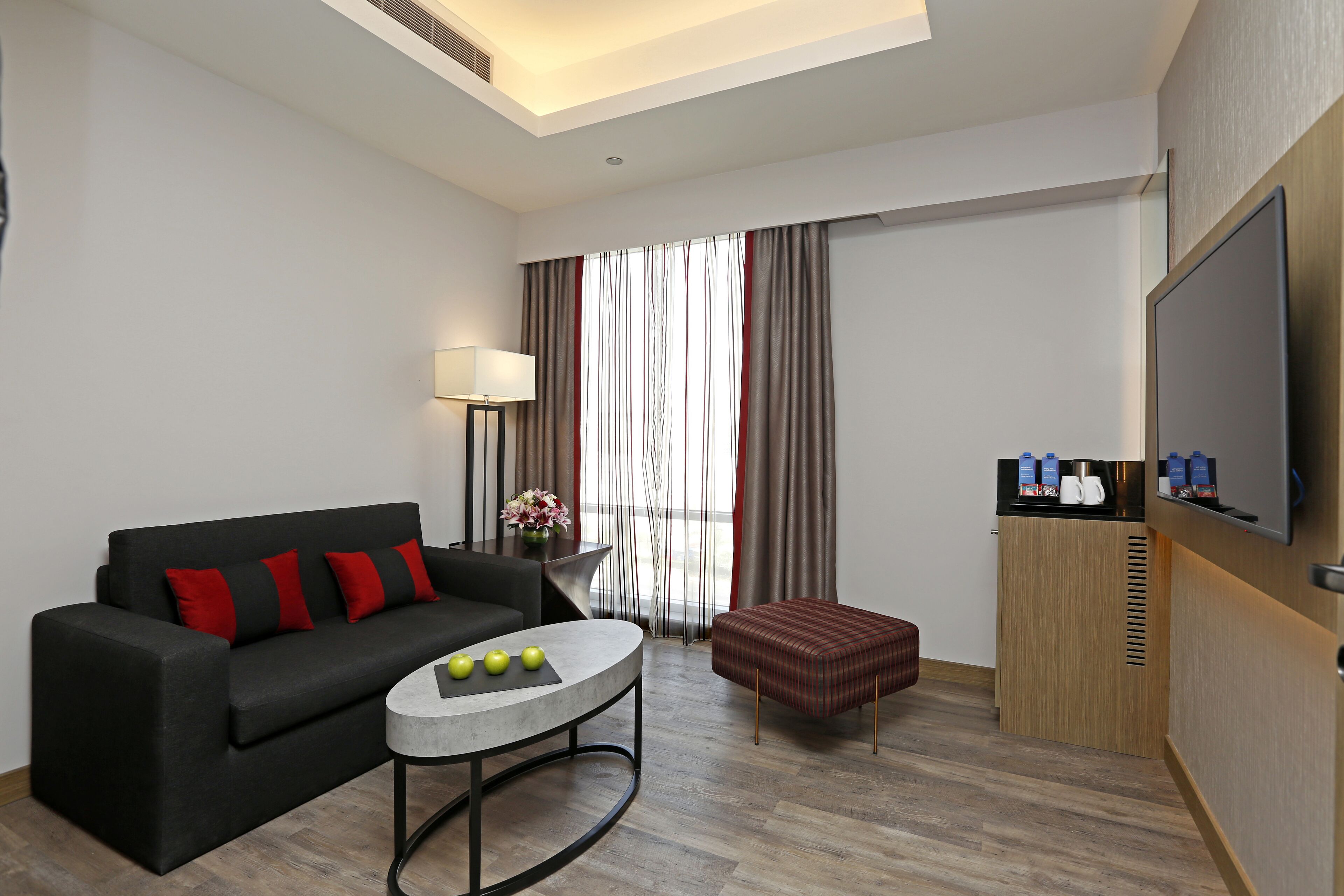 Una habitación de hotel moderna con un sofá, una mesa redonda para café, un televisor y un minibar.