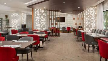 A modern dining area with wooden tables and chairs, a large TV screen, and decorative panels.
