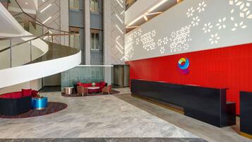 Un vestíbulo moderno con una escalera curva, un mostrador de recepción y una zona de estar con un sofá rojo y una mesa de centro azul.