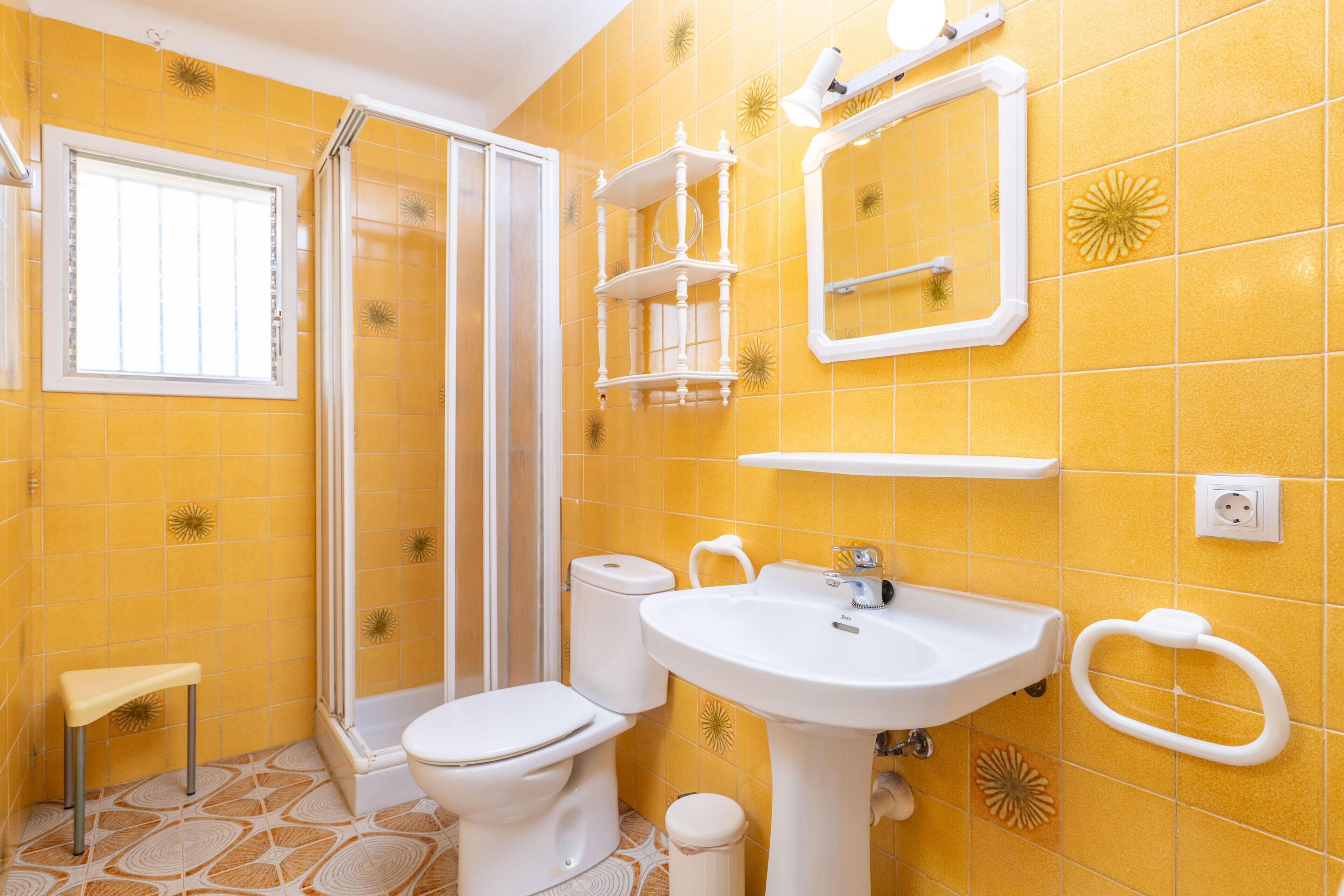 A bathroom with yellow tiles, a toilet, a sink, a mirror, and a shower.