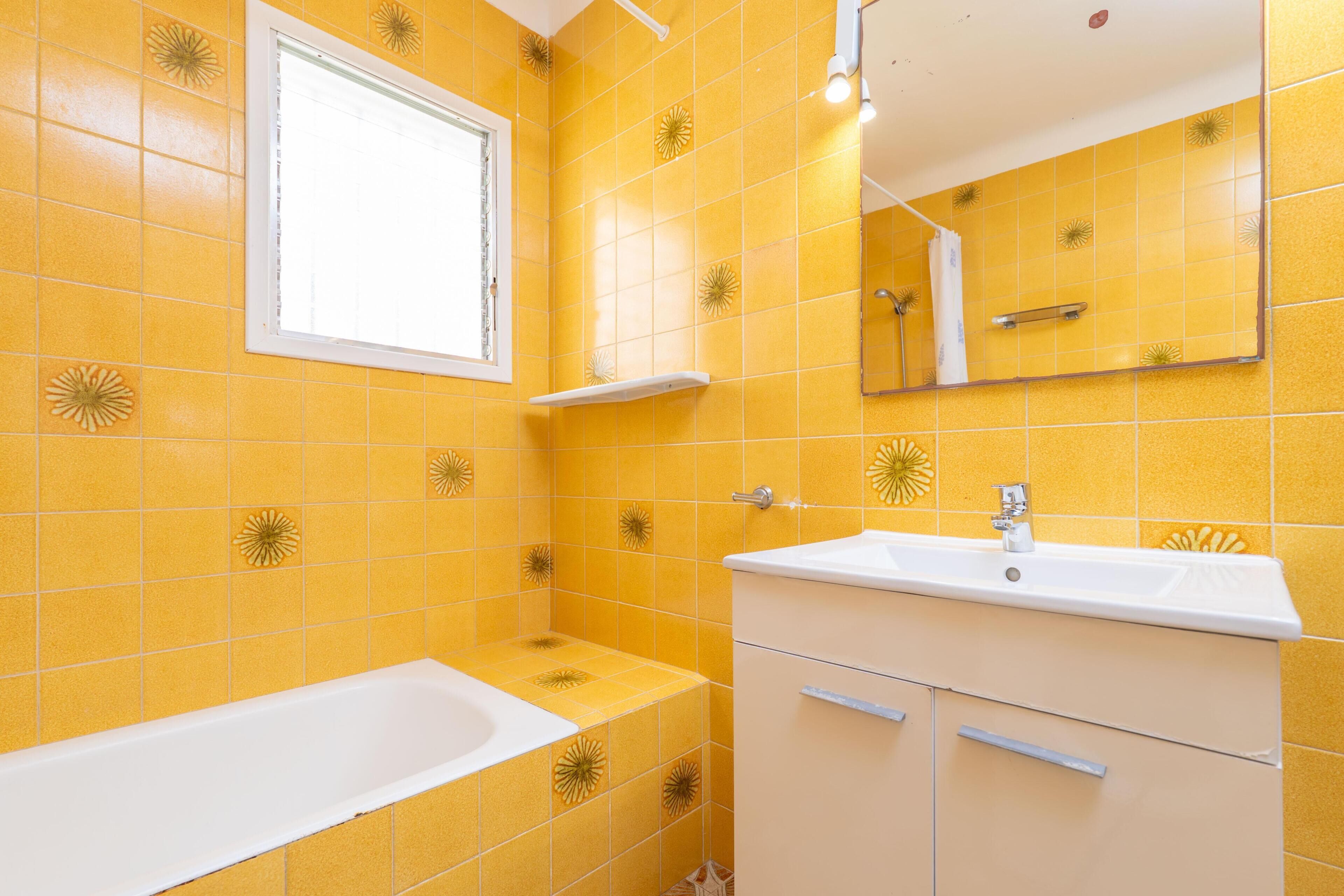 A bathroom with yellow tiles, a white bathtub, a sink with a mirror above it, and a shower area.