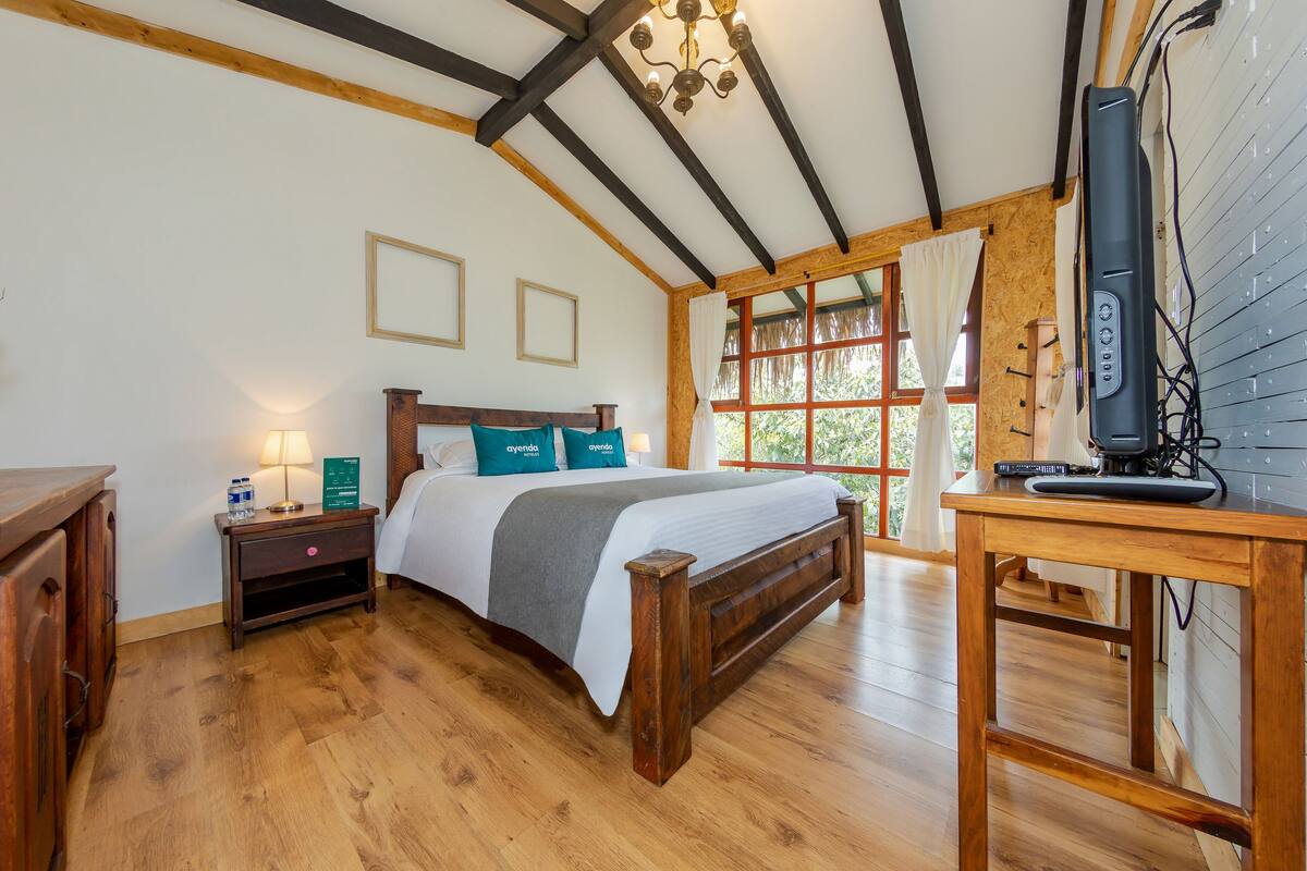 A wooden-framed room with a bed, bedside table, and a desk with a computer.