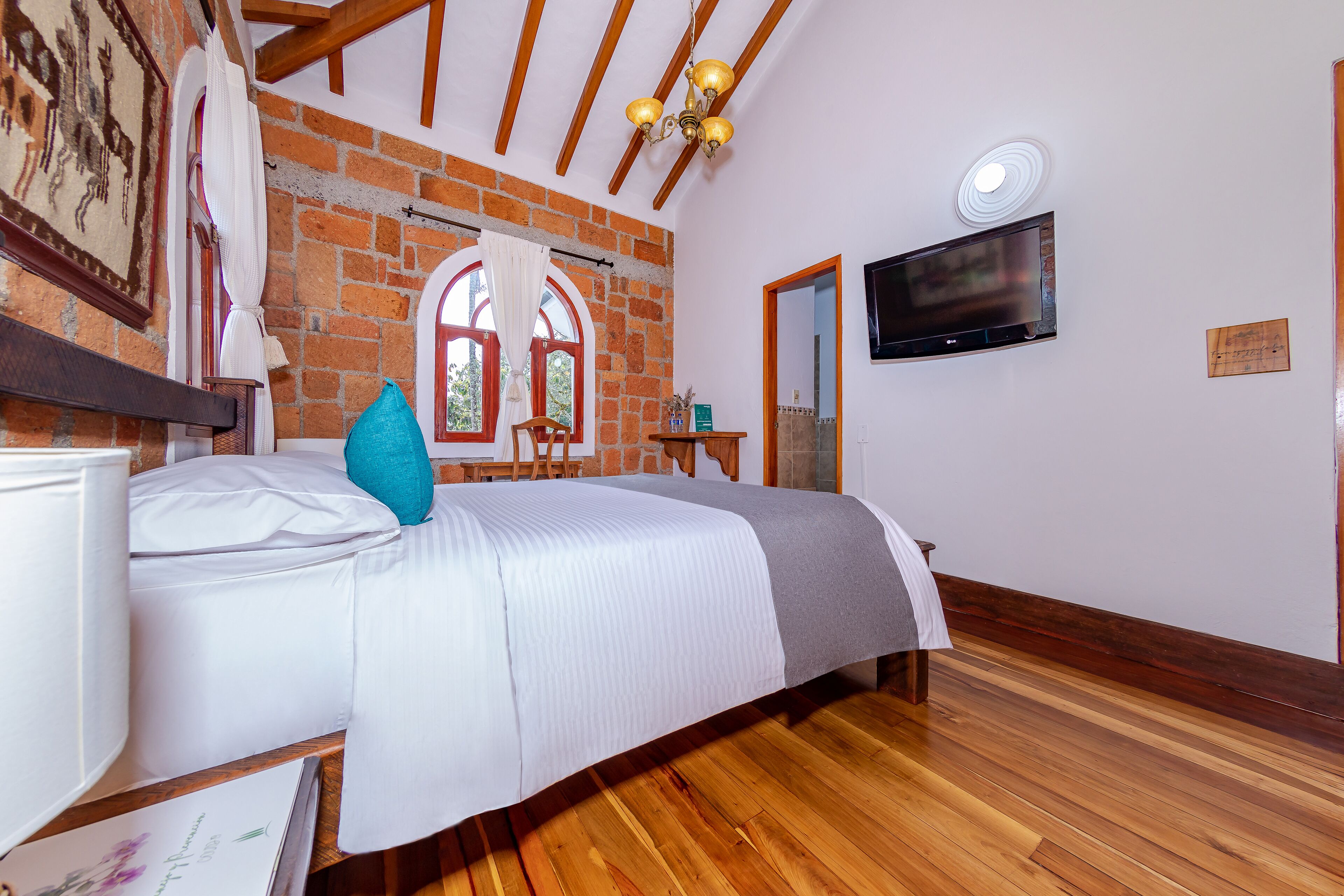 Ein Schlafzimmer mit Bett, Holzboden, Backsteinwand, Fernseher und einem kleinen Tisch mit Stuhl.