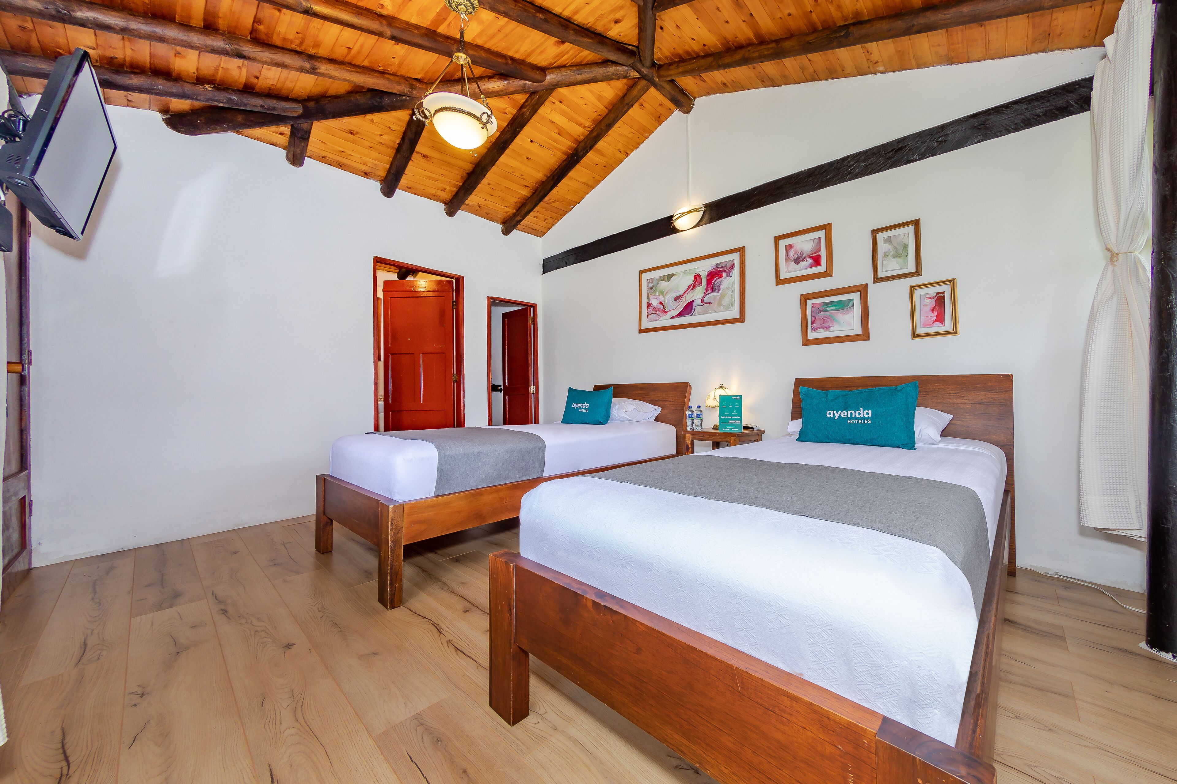 A room with two wooden beds, a wooden ceiling, and a television mounted on the wall.