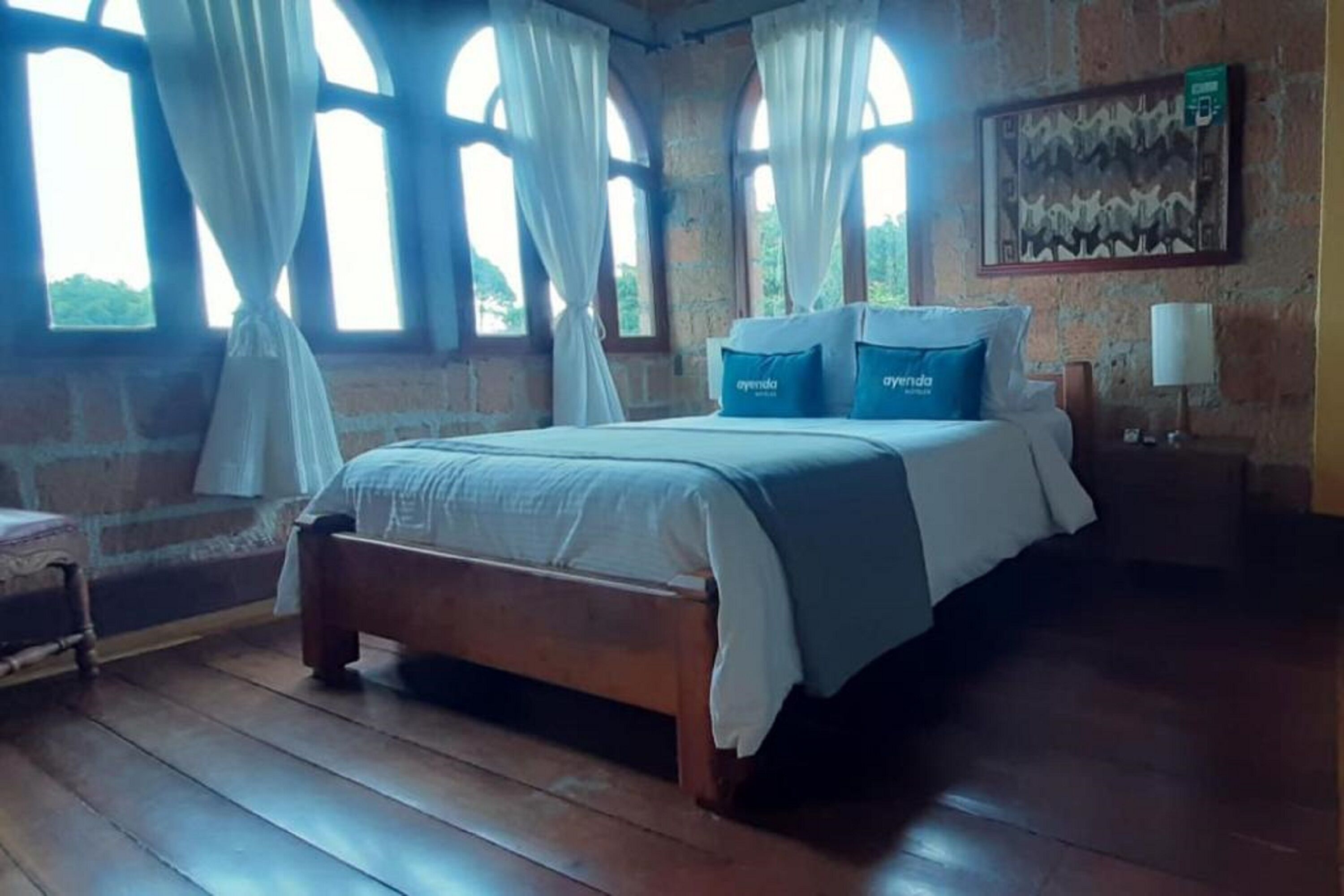 Een slaapkamer met een houten bed, witte gordijnen en een schilderij aan de muur.
