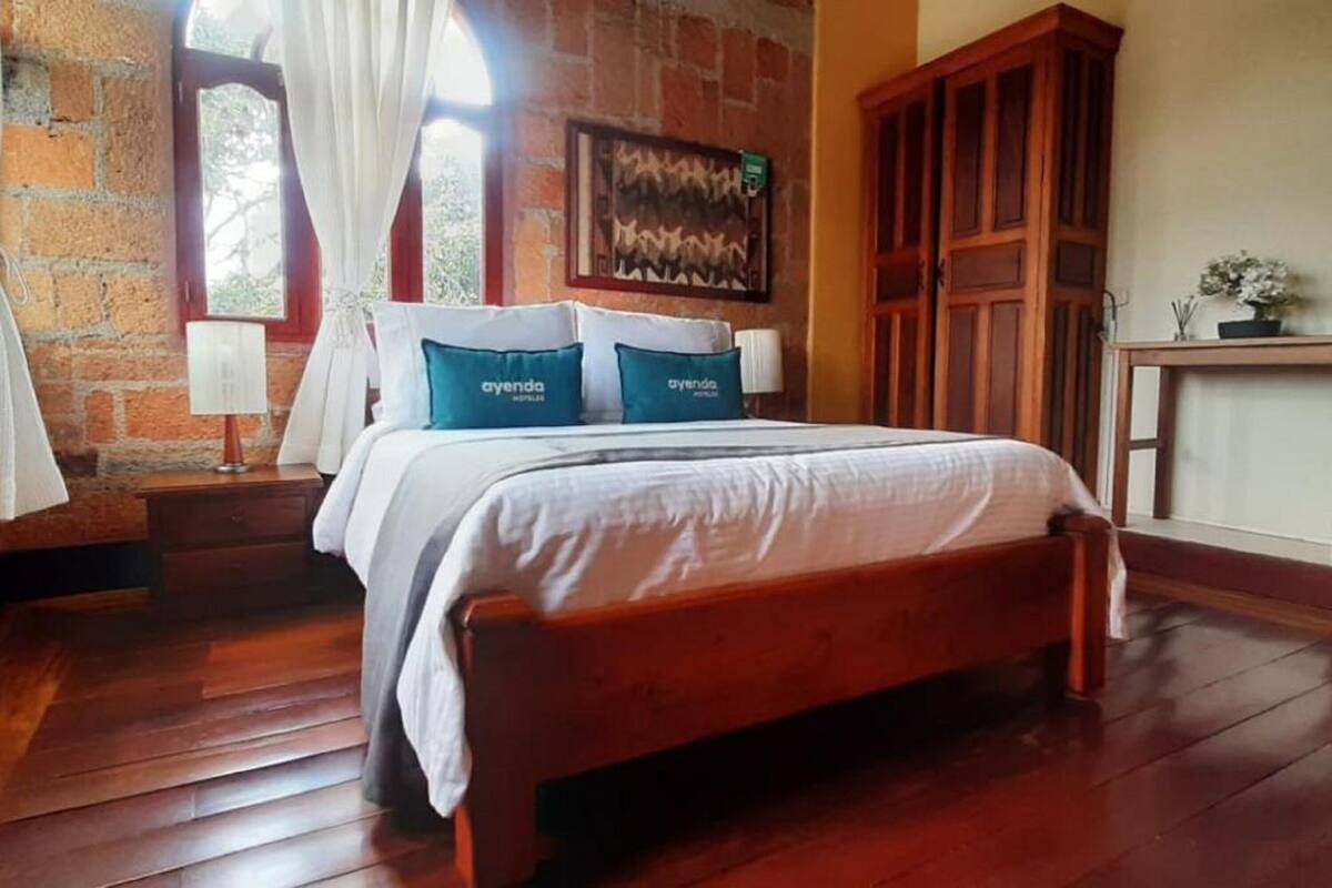 A bedroom with a wooden bed, white bedding, and blue pillows with 'ayenda' text.