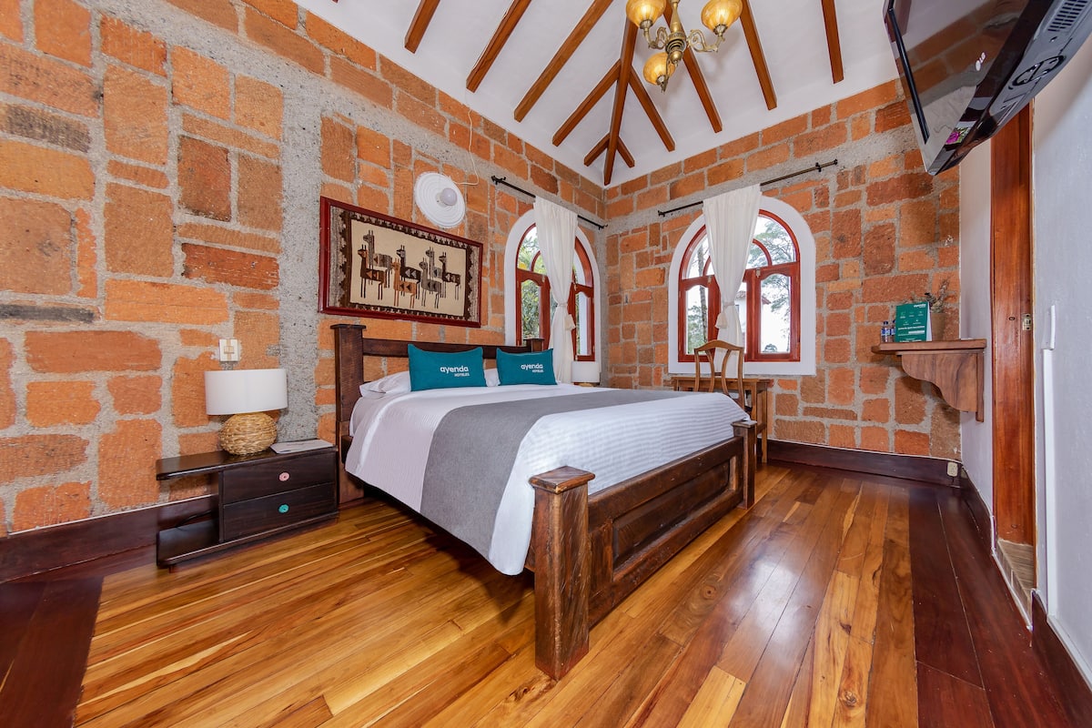 A bedroom with a wooden bed, brick walls, and wooden flooring.