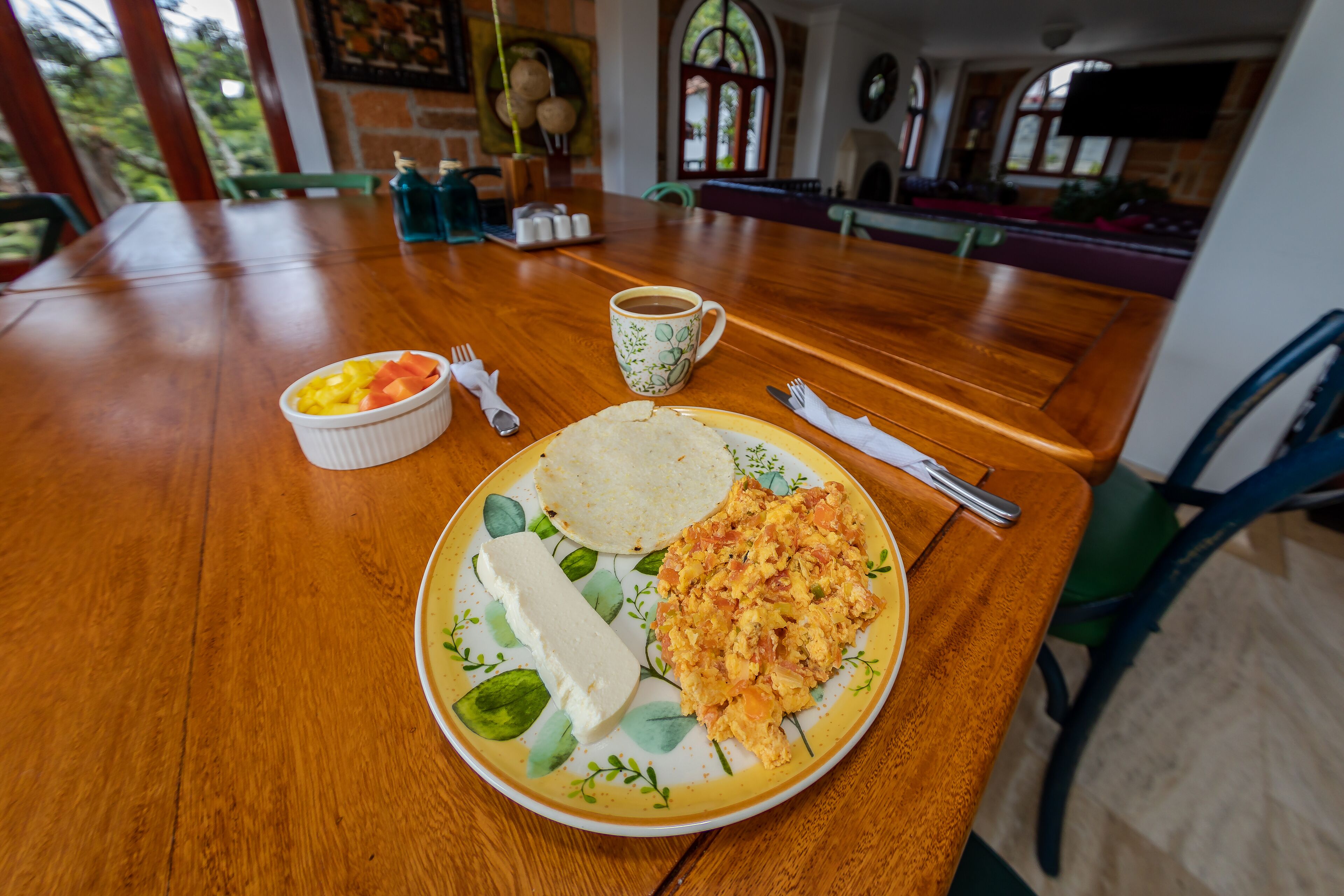 Una mesa de madera con un plato de comida, una taza y cubiertos.