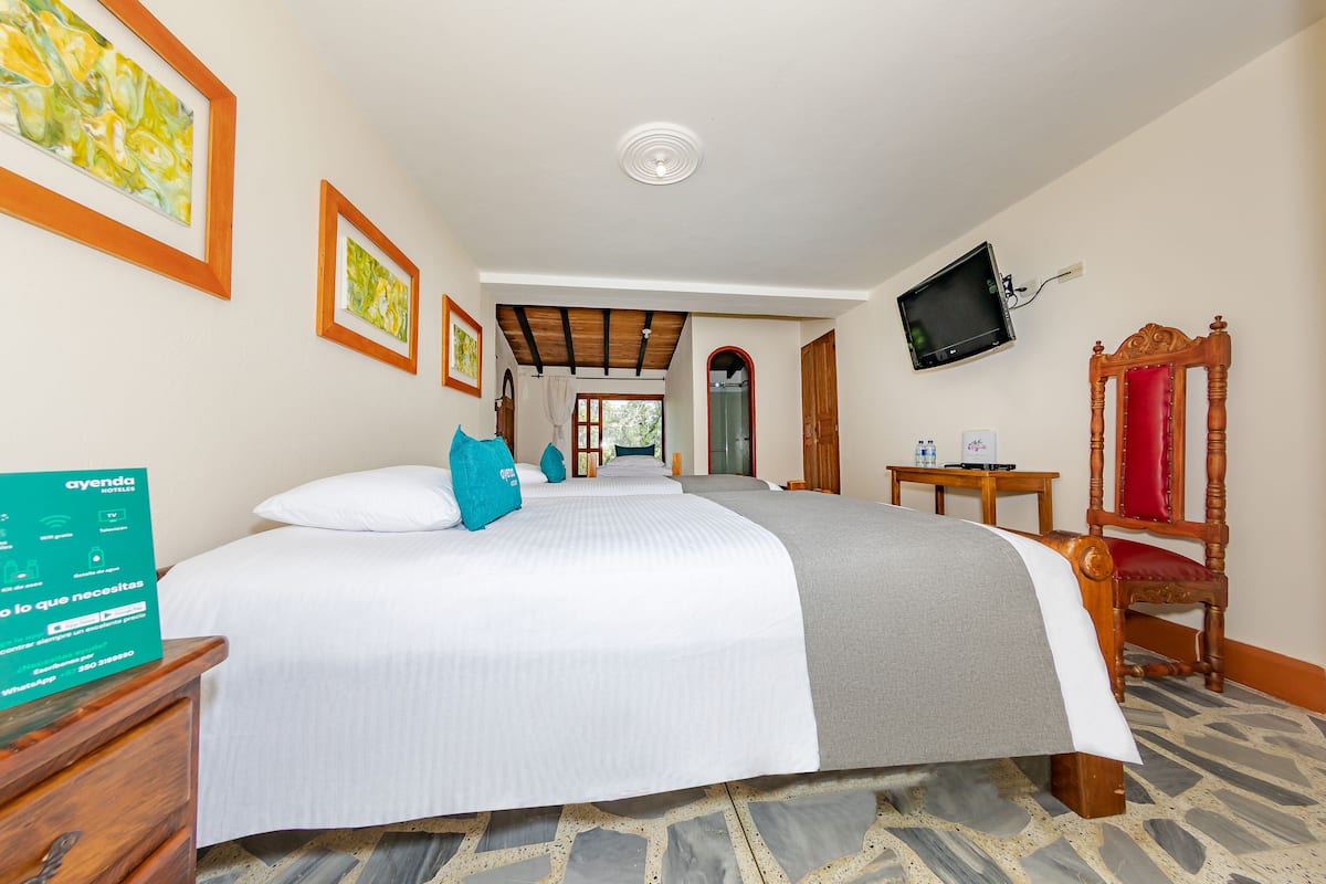 A hotel room with a large bed, a wooden chair, a television mounted on the wall, and a sign on the nightstand.