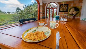 A wooden dining table with breakfast items, a cup, and a view of greenery outside.
