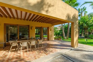 An outdoor patio with a wooden table and chairs, a pergola, and a view of a garden with palm trees. - VILLA SON FLORIANA - House with private pool in Cala Bona Free WiFi (Son Servera)