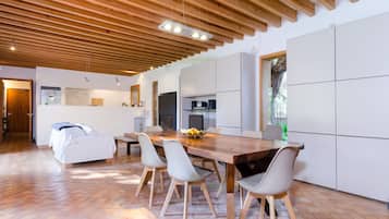 Una cocina moderna con techo de madera, armarios blancos y un comedor con una mesa grande y sillas.