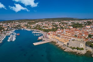 Vista aérea de un pueblo costero con un puerto deportivo, edificios históricos y una imponente fortaleza de piedra.