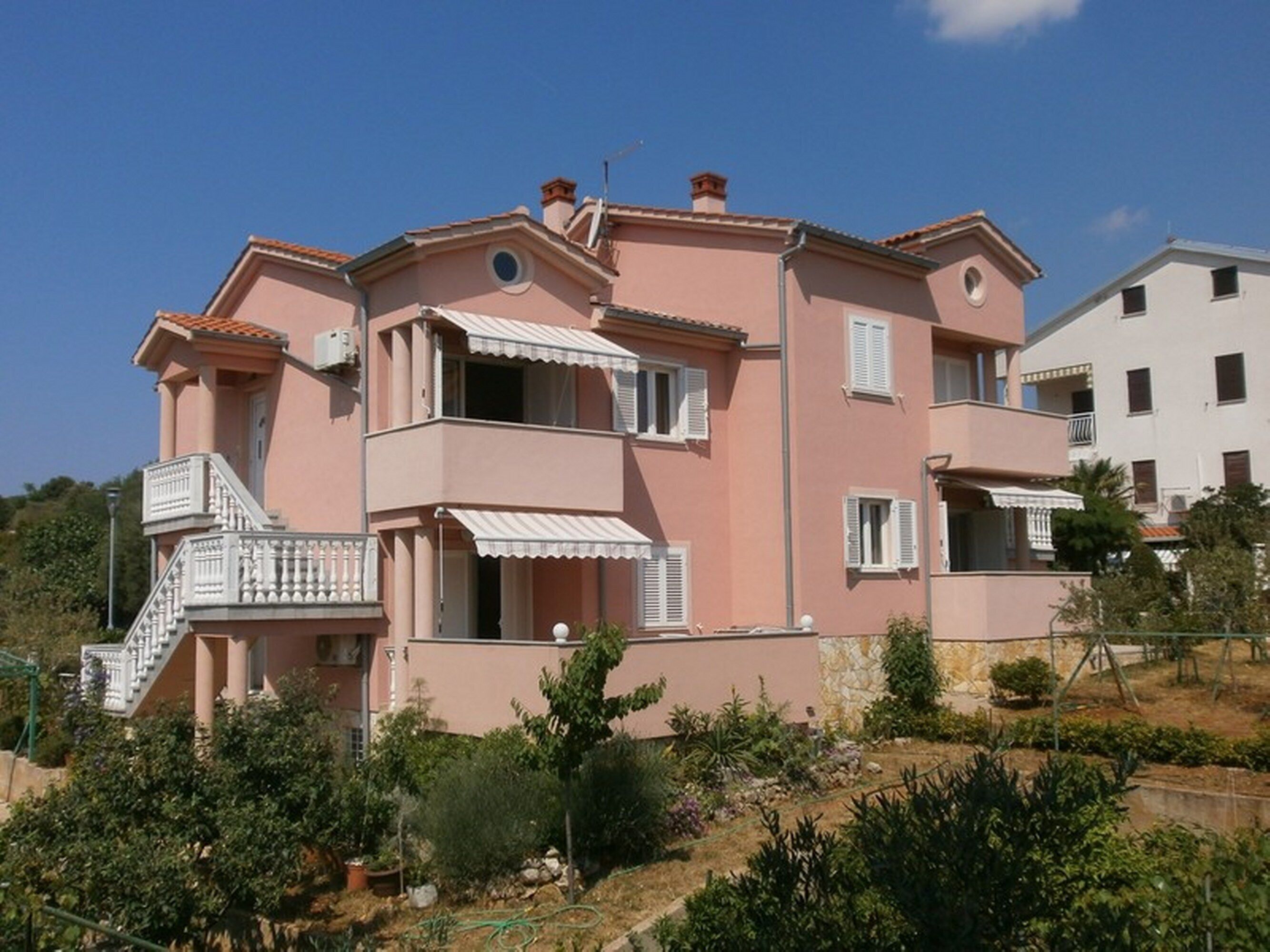 A pink multi-story residential building with balconies, a staircase, and a garden area.