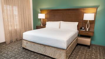 A hotel room with a large bed, two bedside tables, a nightstand, a bench, and a curtain.