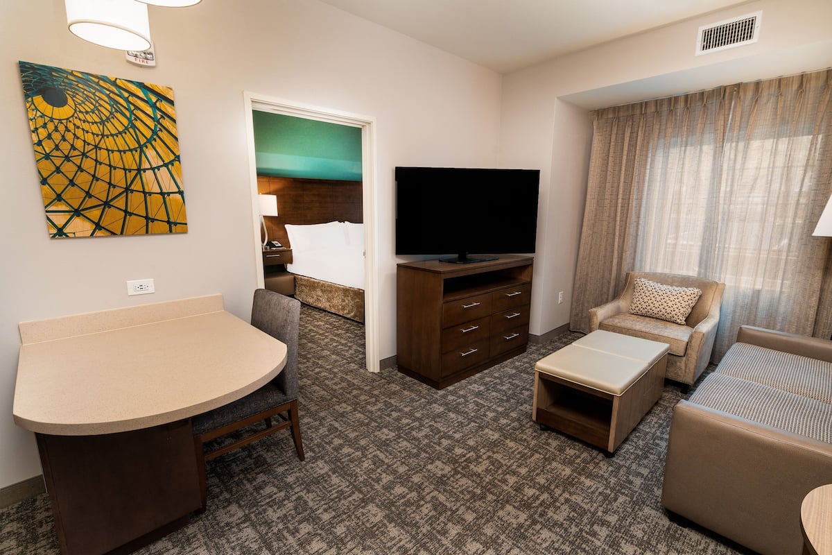 Ein Hotelzimmer mit einem gebogenen Schreibtisch, einem Flachbildfernseher, einer Couch und einem gemusterten Teppich.