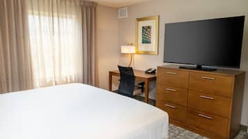 Una habitación de hotel con una cama grande, un escritorio con una silla, un televisor y un aparador de madera.