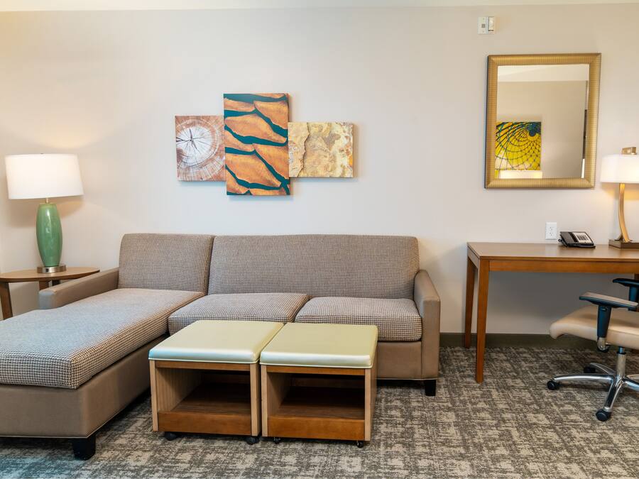 A hotel room with a sofa, a desk, a chair, a lamp, and artwork on the wall.