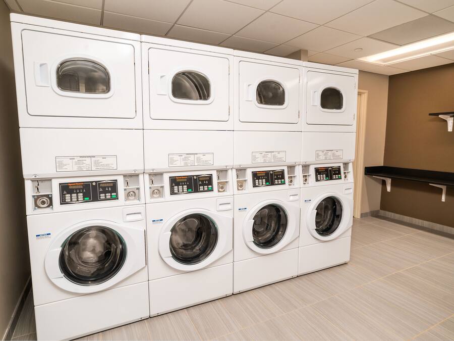 Een rij witte wasmachines met een voorlaadklep in een wasserij, met een betegelde vloer en een bruine muur.