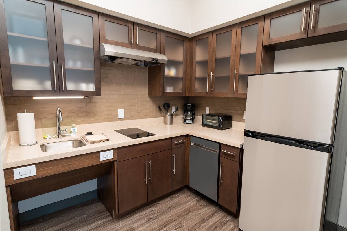Eine moderne Küche mit Holzschränken, einer Edelstahlspüle, einem Geschirrspüler, einem Toaster und einem Kühlschrank.