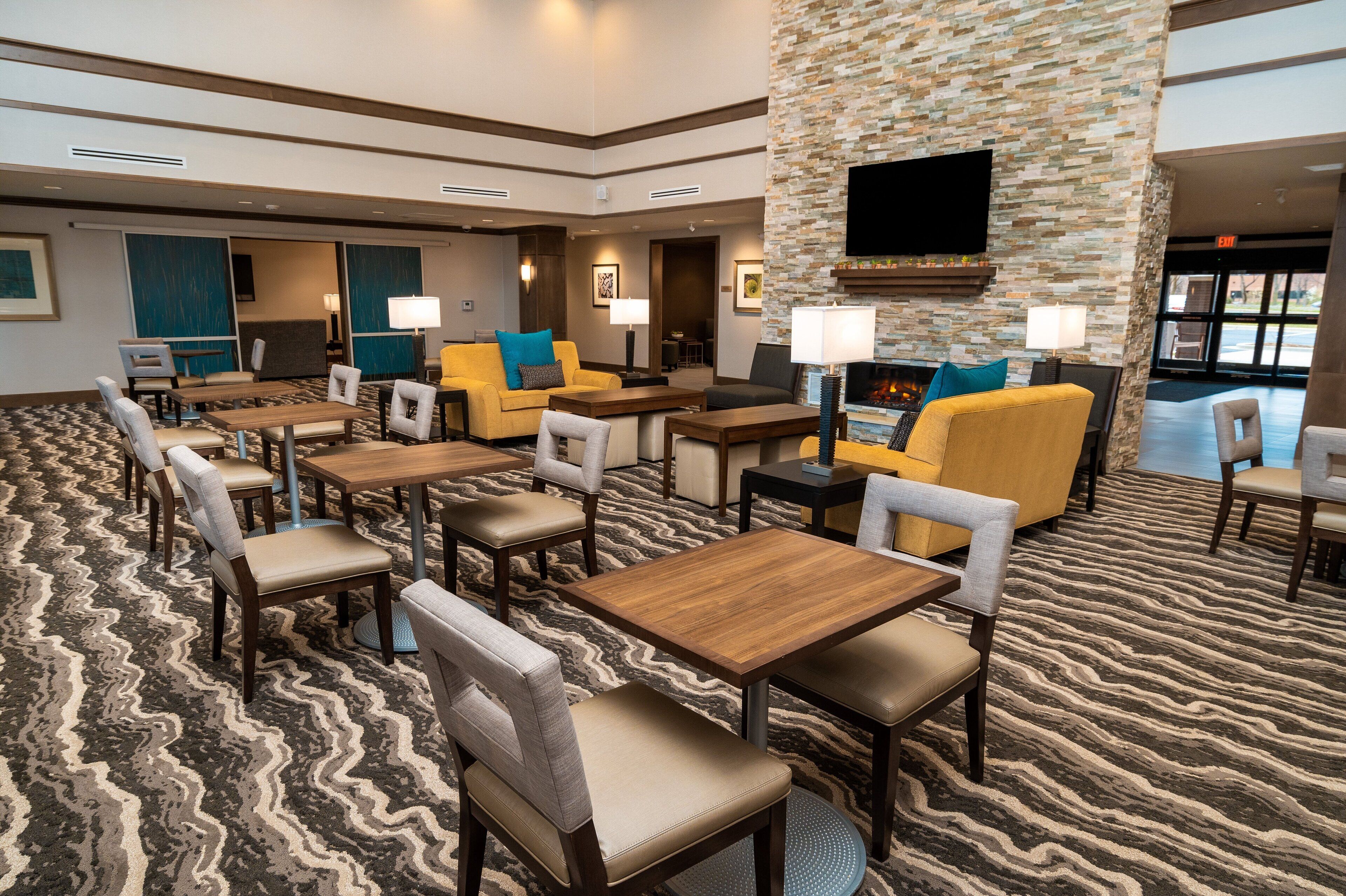 A hotel lobby with multiple seating areas, a fireplace, and a flat-screen TV mounted on a stone wall.