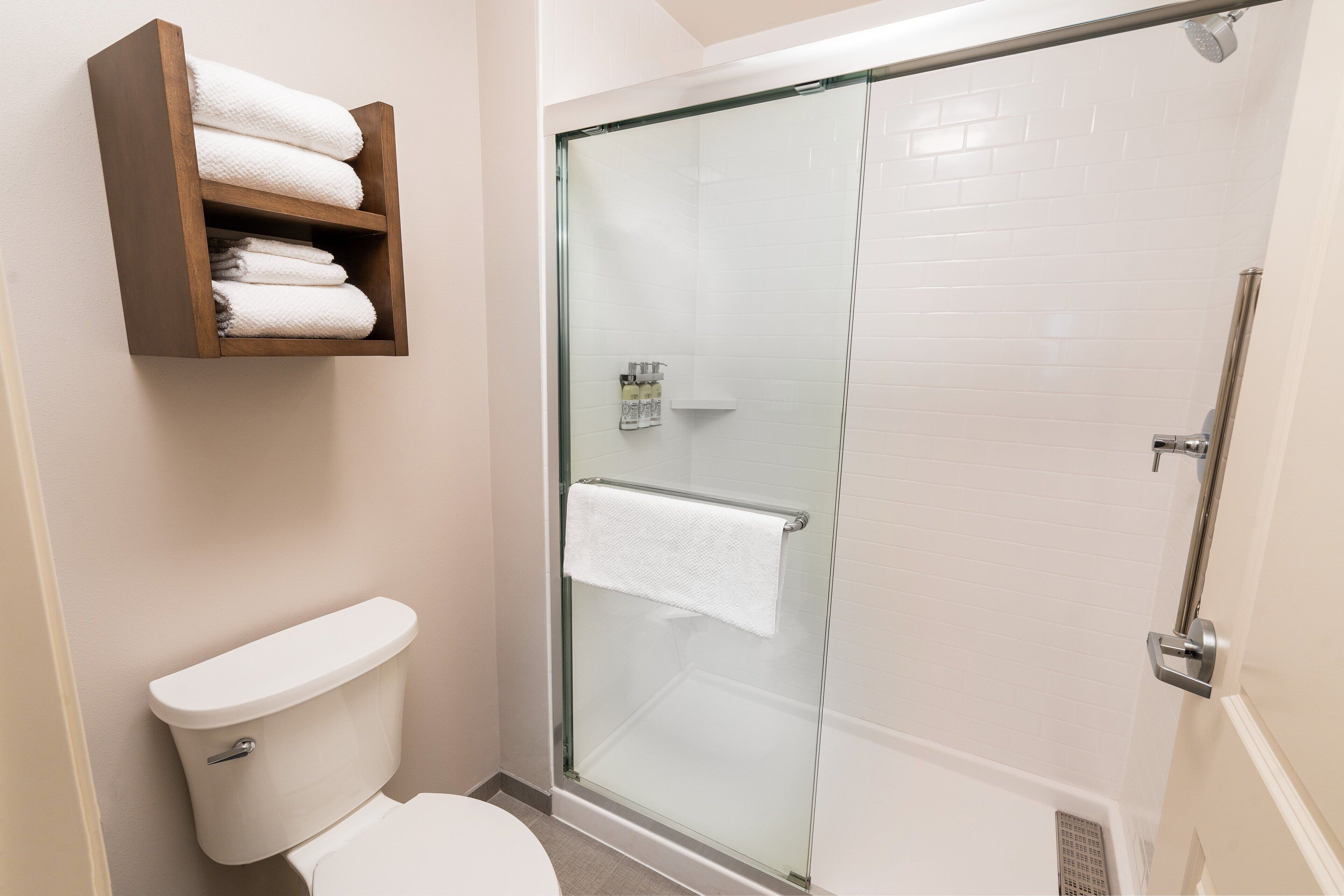 Un baño con ducha de vidrio, inodoro y estante de madera con toallas.