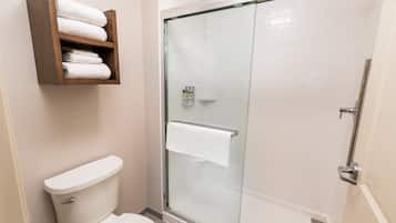Un baño con ducha de vidrio, inodoro y estante de madera con toallas.